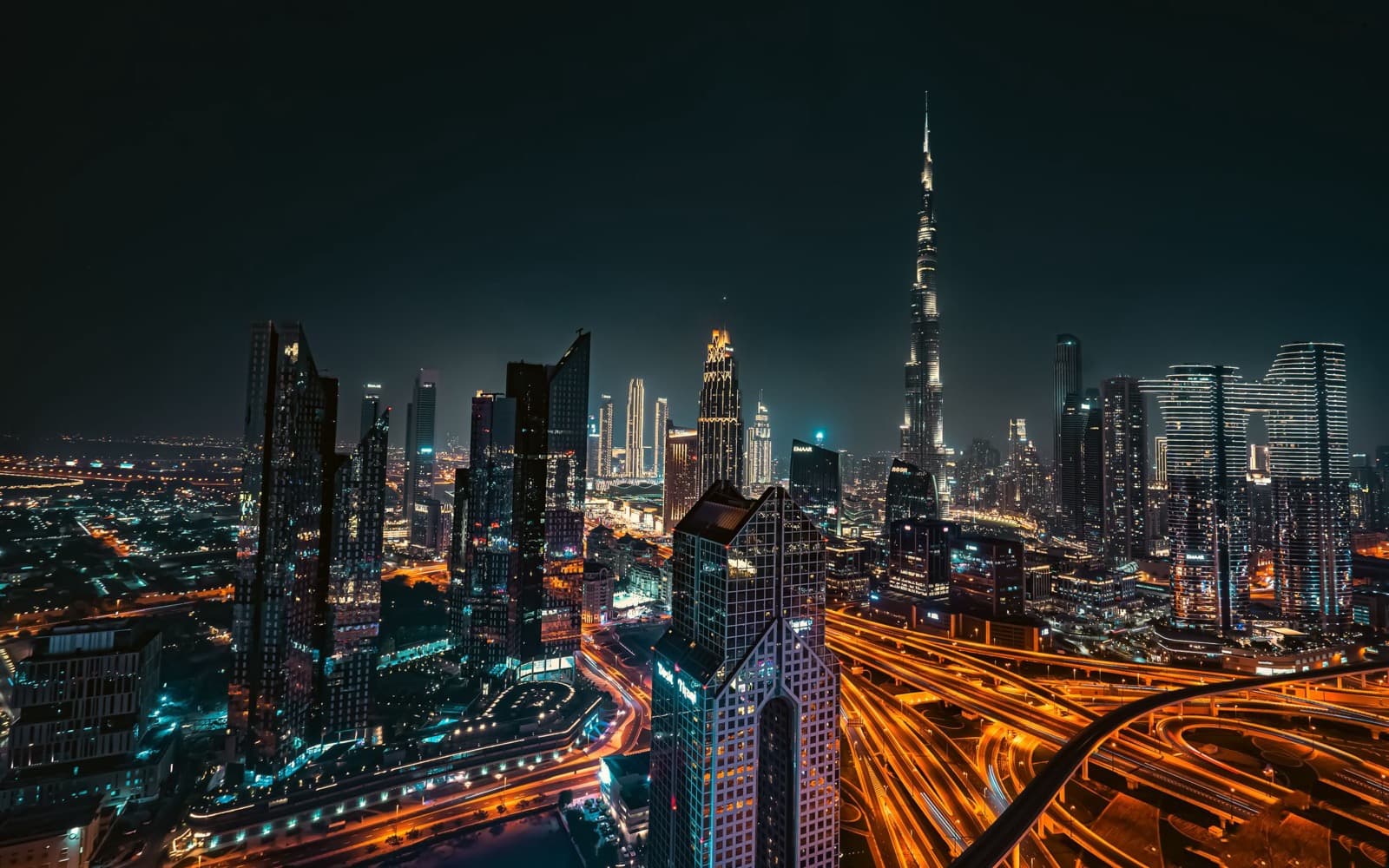 Downtown Dubai skyline at night with the Burj Khalifa above lit towers and highway light trails