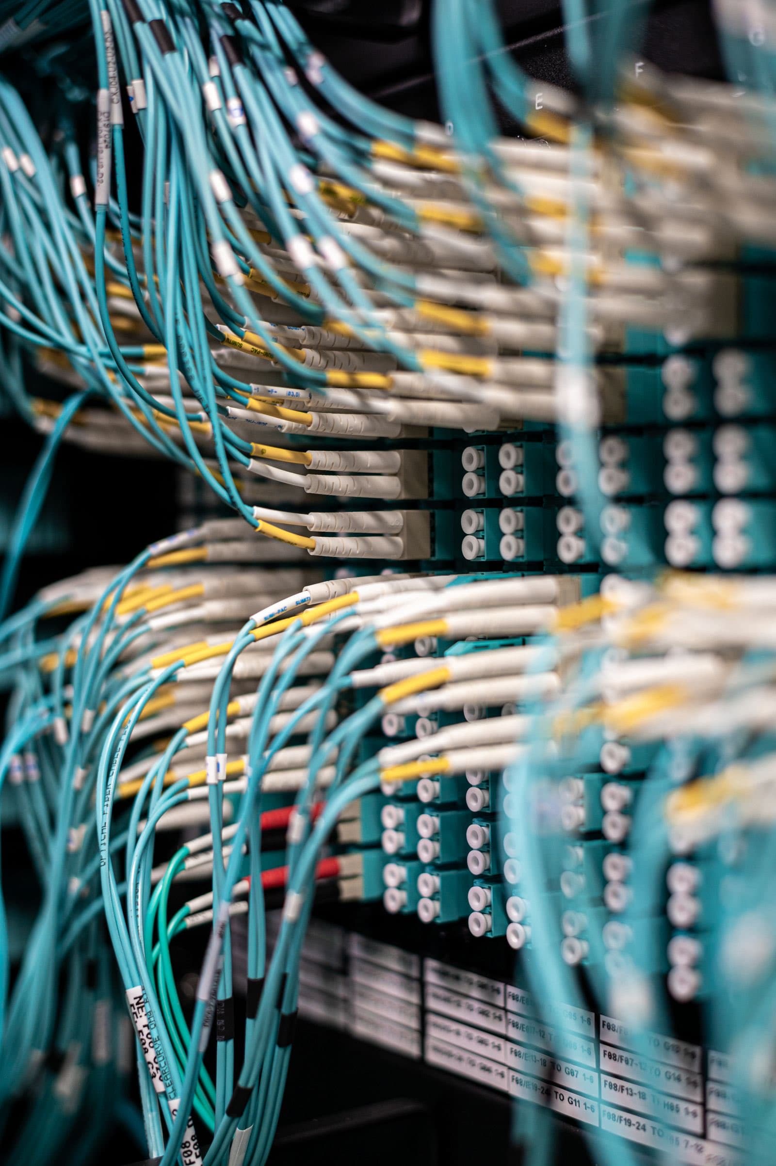 Dense aqua fibre-optic patch cables terminating into LC connector panels in a data centre